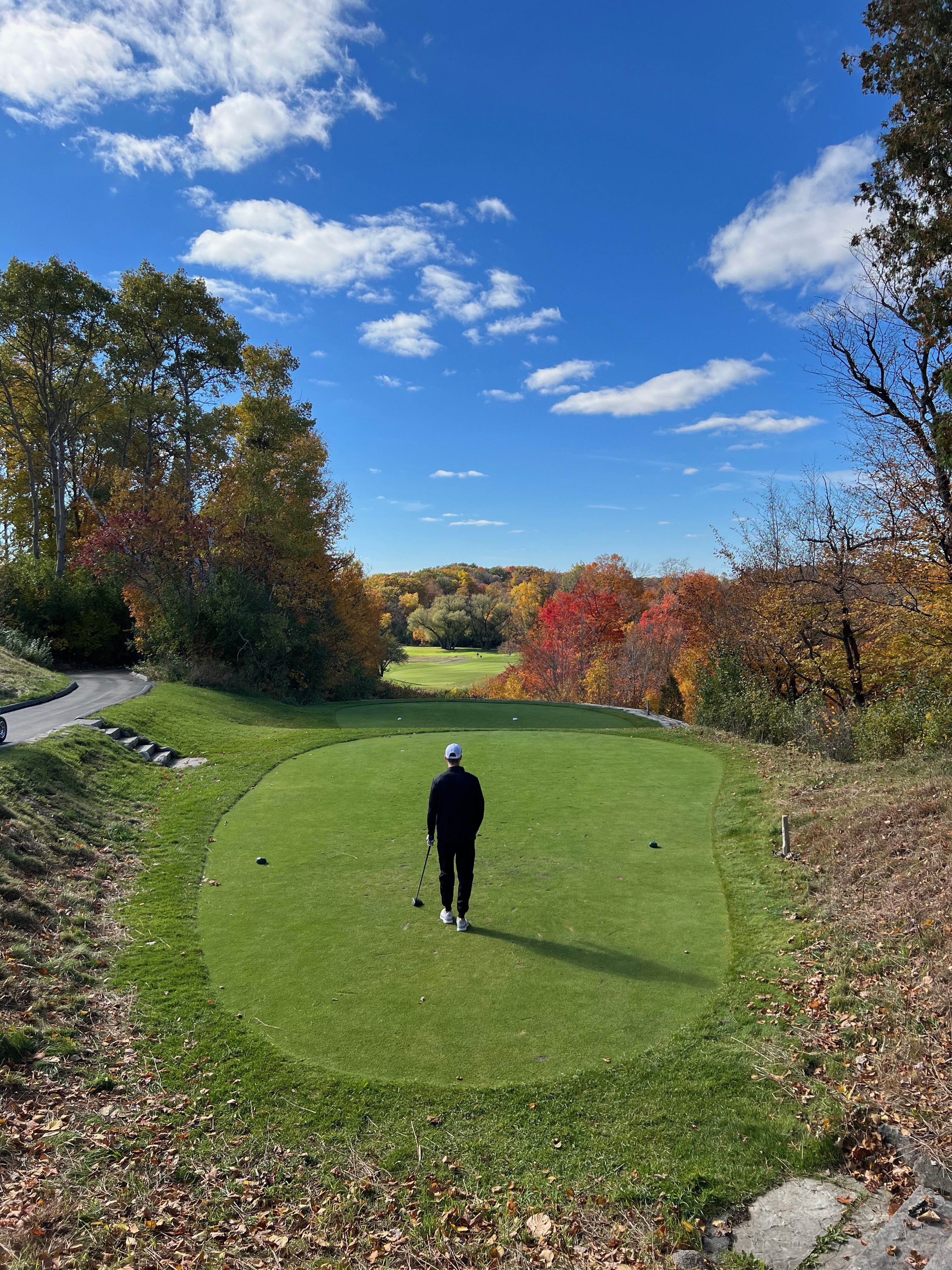 A golfer standing on a scenic golf course during autumn, surrounded by colorful fall foliage